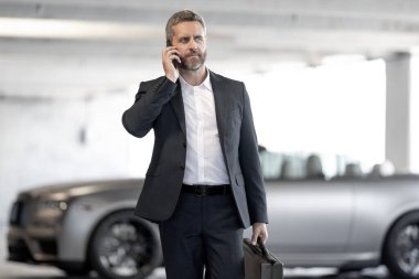 Lüks bir arabanın yanında zengin bir işadamı. Açık havada başarılı bir iş adamı. Zarif zengin iş adamı. Pahalı arabası olan bir patron. Premium bir arabanın önünde duran bir iş adamı. İş başarısı