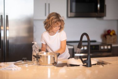 Çocuk mutfak içinde bulaşık yıkıyor. Çocuk, anne ve babasına ev işlerinde yardım ediyor. Mutfakta bulaşık yıkamada çocuk yardımı