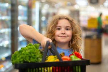 Marketteki çocuk. Sebze dolu alışveriş arabası olan çocuk. Çocuk sebzeleri markette seçiyor. Çocuk bakkaldan alışveriş yapıyor. Çocuklar için market eğlencesi. Meyve dükkanındaki çocuk