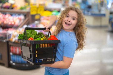 Marketteki çocuk. Çocuk markette meyve seçiyor. Çocuklar için market eğlencesi. Çocuk markette taze meyve topluyor. Markette elinde sebze sepeti olan genç bir müşteri. Çocuk marketten alışveriş yapıyor.