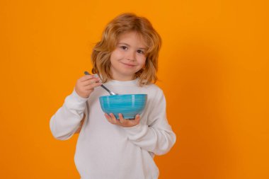 Çocuk kaşık ve kase ile kahvaltı yapıyor. Komik çocuk lezzetli süt ürünlerinin tadını çıkarıyor. Elinde bir fincan organik yiyecek tutan çocuk. Sağlıklı yemekle birlikte çocuk portresi. Genç çocuk taze yemek yiyor. Çocuklar için sağlıklı yemek