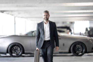 Lüks arabanın yanında zengin bir işadamı. Başarılı iş adamı. Şık ceketli, olgun, zengin bir iş adamı. Takım elbiseli zengin bir iş adamı dışarıda yürüyor. Lüks başarılı iş adamı