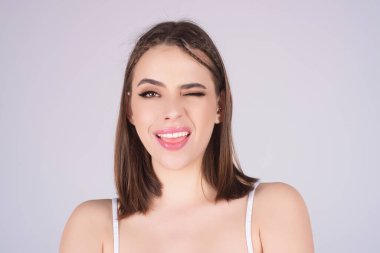 Güzel kız göz kırpıyor. Göz kırpan genç bir kadının yakın plan portresi. Göz kırpan komik bir ifade. Olumlu duygular gösteren kadın. Şakacı yüz hareketi yapan bir kız. Komik surat. Göz kırpan kız portresi