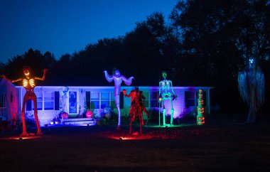 Cadılar Bayramı evinin dışında ürkütücü bir dekor var. Ön bahçede korkunç bir iskelet var. Ürkütücü fenerler ve balkabaklarıyla dekore edilmiş bir ev. Cadılar Bayramı süsü verandada. Geceleri ürpertici ev görüntüsü