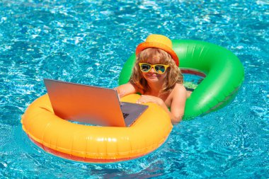 Çocuk yaz havuzunda dizüstü bilgisayarla çalışıyor. PC kullanan küçük serbest çalışan, havuz başında çalışan
