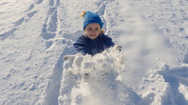 Çocuk kar atıyor. Kış eğlencesi. Kar atan mutlu çocuk. Çocuklar kartopu atarak karda oynarlar. Karda oynayan çocuk, kış doğasında tatil. Örgü şapkalı çocuğun kış portresi.