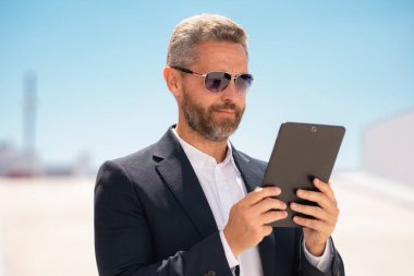 Dışarıda tablet kullanan bir iş adamı. Tabletli başarılı bir iş adamı. Şirket lideri iş adamı tablet üzerinde çalışıyor. Zarif iş adamı tableti kontrol ediyor. İş adamı belgeleri inceliyor