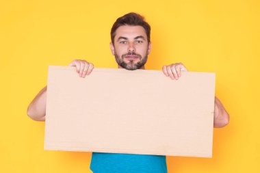 Stüdyonun arka planında boş tahtası olan yakışıklı bir adam. Telif uzayı ile boş tabela gösteren bir adam. Fikir teklifi. Reklamınız. Metin için boş alanı olan boş reklam panosu, modelle