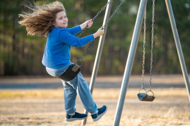 Bahar parkında sallanan neşeli çocuk. Sarı saçlı küçük bir çocuk salıncakta sallanıyor. Parkta gülümseyen mutlu çocuk. Mutlu çocukluk anları. Çocuk dışarıda oynuyor. Çocuk salıncakta eğleniyor. Çocuklar için açık hava oyunu