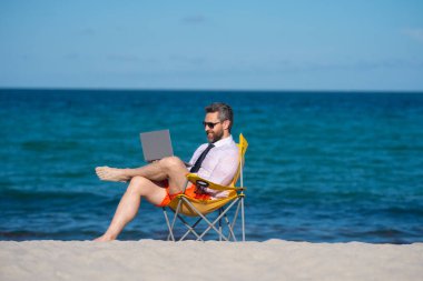 Deniz sahilinde dizüstü bilgisayar kullanan iş adamı. Yaz tatilindeki çılgın iş adamı. Heyecanlı iş adamı, çılgın komedi dünyası konsepti. Uzaktan kumanda çalışıyor. Yaz iş hayalleri