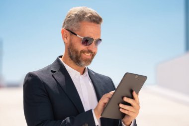 Açık havada tablet kullanan mutlu bir iş adamı. Tabletle başarılı bir iş adamı. Dışarıda tablet üzerinde çalışan bir iş adamı. Zarif iş adamı tableti kontrol ediyor. Dijital aygıt kullanan işadamı