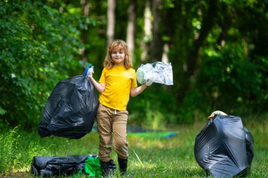 Çöp poşeti dolusu çöp ve çöp maşası olan bir çocuk. Geri dönüşüm kutusuyla ormanda veya parkta plastik atık toplayan sevimli bir çocuk. Çevre aktivistleri. Çevresel koruma ve ekoloji