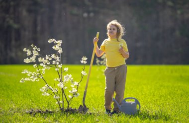 Bir çocuk dikme ağacı portresi. Çocuk bahçıvan. Bahçede çalışan bir çocuk. Çevre için büyüyen ağaç ve bakım bitkisi. Ekim mevsimi. Bitki yetiştiren bir çocuk. Bahçe işleri.