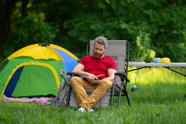 Adam doğada kamp yapmayı seviyor. Kamp gezisi. Yürüyüşten sonra bir çadırda dinleniyor. Huzurlu bir kamp alanında tatil. Yazın piknik. Açık hava macerasının özgürlüğü. Erkek kampı ve rahatlama