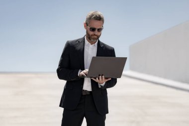 İş adamı dışarıda dizüstü bilgisayar kullanıyor. Dizüstü bilgisayarda çalışan başarılı bir adam. Dizüstü bilgisayarı olan kendinden emin bir iş adamı. İnternette iş. İş adamı laptoptaki verileri kontrol ediyor. Takım elbiseli iş adamı internette çalışıyor.