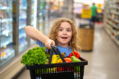 Marketteki çocuk. Çocuk markette meyve seçiyor. Çocuklar için market eğlencesi. Çocuk markette taze meyve topluyor. Markette elinde sebze sepeti olan genç bir müşteri. Çocuk marketten alışveriş yapıyor.