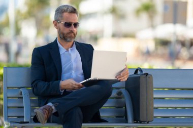 Açık havada dizüstü bilgisayar üzerinde çalışan başarılı bir iş adamı. Kendine güvenen bir iş adamı elinde dizüstü bilgisayarla bankta oturuyor. İspanyol iş adamı uzaktan çalışıyor. Zengin iş adamı yazın internette çalışıyor.