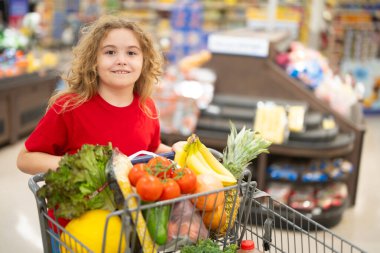 Markette alışveriş arabasıyla çocuk alışverişi. Çocuk markette taze sebze seçiyor. Markette yiyecek alışverişi yapan çocuk. Yerel bir dükkanda sağlıklı ürünler seçen bir çocuk. Bakkalda taze yiyeceği olan çocuk.