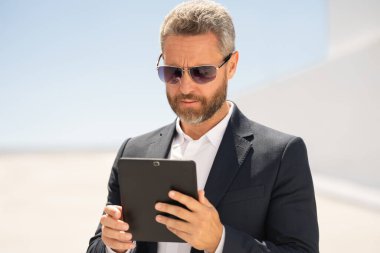 Ciddi bir iş adamı dışarıda tablet kullanıyor. Tabletle başarılı bir iş adamı. Dışarıda tablet üzerinde çalışan bir iş adamı. Zarif iş adamı tableti kontrol ediyor. Dijital aygıt kullanan işadamı