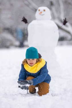 Çocuk kışın kardan adam için kartopu yapıyor. Çocuk karda oynuyor. Açık havada aktif kış oyunları. Çocuk karla oynarken eğleniyor. Çocuklar için açık havada kış tatili. Güneşli kış gününde çocuk oyunu