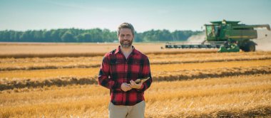 Hasat zamanı. Tarlada çalışan çiftçi. Kırsalda çiftçilik. Hasat tarlaları olan çiftlik arazisi. Olgun arpa toplayan çiftçi. Çiftçi hasatı kontrol ediyor. Çiftçi hasatı inceliyor.