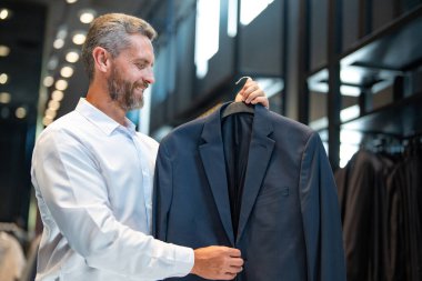 Takım elbiseli, takım elbiseli bir adam. Bir iş adamı mağazada şık bir takım elbise seçer. Modayı takip eden bir müşteri resmi kıyafet alırken ceketi inceler. Klasik kıyafetli çekici bir manken.