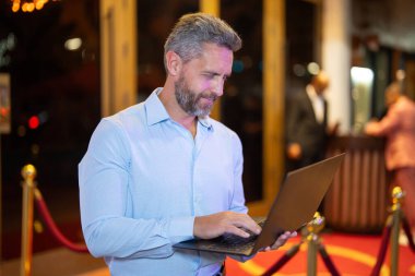 Gece lambasında dizüstü bilgisayar kullanan bir iş adamı. İşadamı sokakta dizüstü bilgisayarda çalışıyor. Gece kulübü yakınlarında orta yaşlı bir iş adamı iş planlıyor. İş 40 'larda. Serbest Çalışan açık havada dizüstü bilgisayarda geziniyor