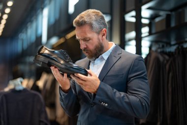 Takım elbiseli şık bir adam bir butikte lüks ayakkabılara hayran. Bir iş adamı bir ayakkabı mağazasında şık ayakkabılar seçer. Resmi görünmek için klasik deri ayakkabılar. Resmi ayakkabılar