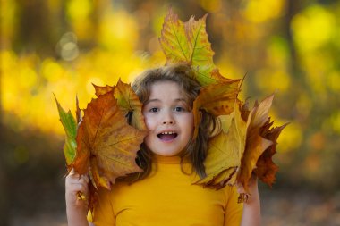 Akçaağaç yapraklı çocuklar arka planda. Sonbahara yakın bir çocuk güneş ışığında yapraklarını döküyor. Sonbahar sonbahar parkında küçük bir çocuk. Çocuklar ve yapraklar, dökülen yapraklar. Sonbahar yaprağı. Düşen yapraklar