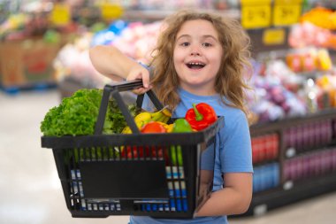 Çocuk bakkaldan alışveriş yapıyor. Çocuk markette meyve seçiyor. Sebzeli alışveriş. Çocuklar için market eğlencesi. Çocuk taze meyve topluyor. Süpermarketteki çocuk. Sepet dolusu sebzeli çocuk.