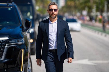 Zengin bir iş adamı. Zengin işadamı başarısının tadını çıkarıyor. Şık takım elbiseli lüks iş adamı. Pahalı arabanın önündeki zengin adam. Lüks iş seyahati. Klasik takım elbiseli, kendinden emin zengin bir iş adamı.