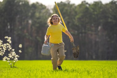 Bahçede ağaç yetiştiren bir çocuk. Çocuk kürekle toprak kazıyor ve ağaç dikiyor. Çocuk bahçıvan meyve ağaçları yetiştiriyor. Çocuklarla ağaç yetiştirmek. Çocuklar için bahçe işleri. Kürekli çocuk ağaç yetiştiriyor.