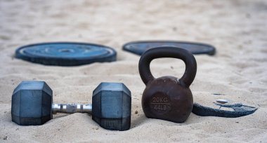 Kettlebell ve ağırlık arka planı. Ağır ağırlıklarla vücut geliştirme. Dambıllarla park egzersizi. Ağırlıklarla spor sahnesi. Kettlebell, halterler ve halterler. Ağırlık çalışması.