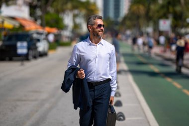 İş adamı şehirde güvenle yürüyor. Sokakta yürüyen bir iş adamı. Ofise doğru yürüyen yakışıklı bir iş adamı. Kendine güvenen girişimci iş adamı dışarıda yürüyor.