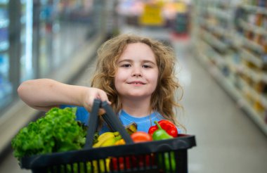 Marketteki çocuk. Çocuk markette meyve seçiyor. Çocuklar için market eğlencesi. Çocuk markette taze meyve topluyor. Markette elinde sebze sepeti olan genç bir müşteri. Çocuk marketten alışveriş yapıyor.