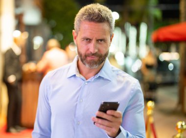 Gece sokakta telefonda konuşan bir iş adamı. İş adamı cep telefonu kullanıyor. Olgun iş adamı internette sohbet ediyor. İş adamı bir arama yapıyor. Şehir işi. İş adamı dışarıda telefonla konuşuyor.