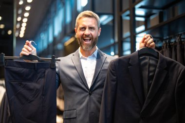 İş adamı için uygun. İyi giyimli bir erkek model bir butikte poz veriyor. Perakende satış elemanı şık bir adamın mükemmel takımı bulmasına yardım eder. Bir mağaza müdürü şık bir takım elbise ayarlar.