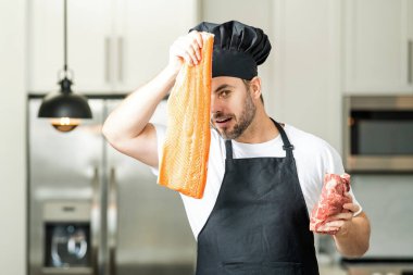 Profesyonel mutfak. Çiğ et ve balık fileto ile şef. Üniformalı adam mutfakta. Şef şapkalı yakışıklı erkek şef mutfakta çiğ et ve balık fileto pişiriyor.