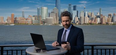 Zengin iş adamı, serbest çalışan. Takım elbiseli bir iş adamı New York 'ta dışarıda dizüstü bilgisayar kullanıyor. Amerikan işi. Manhattan yakınlarında takım elbiseli Amerikalı iş adamları. Açık hava işi. ABD 'de iş