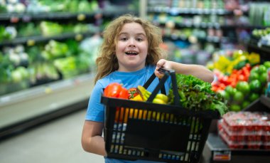 Marketteki çocuk. Çocuk markette meyve seçiyor. Çocuklar için market eğlencesi. Çocuk markette taze meyve topluyor. Markette elinde sebze sepeti olan genç bir müşteri. Çocuk marketten alışveriş yapıyor.