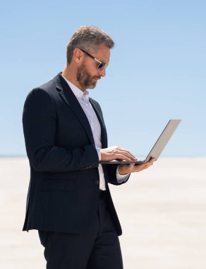İş adamı dışarıda dizüstü bilgisayar kullanıyor. Dizüstü bilgisayar kullanan başarılı bir adam. Dizüstü bilgisayarı olan kendine güvenen bir iş adamı. İnternette iş. İş adamı laptoptaki verileri kontrol ediyor. Takım elbiseli iş adamı internette çalışıyor.