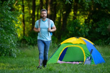 Doğada sırt çantasıyla dolaşan bir gezgin. Doğaya yaz gezisi. Orman kampında dinlenen adam. Kamp gezisi. Yürüyüşten sonra çadırın yanında dinleniyor. Barışçıl bir kamp alanında özgürlük tatili. Piknikteki Adam
