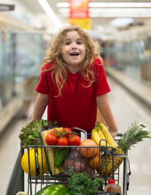 Sepetli çocuk sebze reyonunda. Çocuk markette meyve topluyor. Alışveriş arabalı çocuk. Çocuk süpermarkette alışveriş yapıyor. Çocuk sağlıklı ürünler alıyor. Markette arabası olan bir genç.