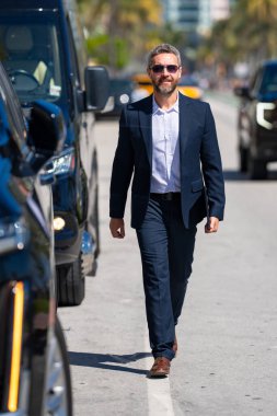 Zengin bir iş adamı pahalı lüks bir arabada. Takım elbiseli zengin bir iş adamı. Şehirdeki başarılı zengin iş adamı. Kendine güvenen bir iş adamı. Başarı işi. İş adamı sokakta yürüyor