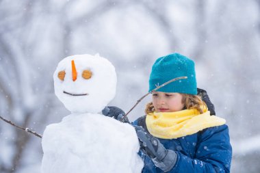 Çocuk kışın kardan adama bakıyor. Kış günü havuç burunlu bir kardan adam. Kardan adam yapan çocuk. Karlı parkta kardan adam yapan küçük çocuk. Karlı kış parkında kardan adamı kucaklayan çocuk