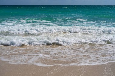 Turkuaz deniz dalgası hareketi. Yaz plajı. Sakin deniz. Deniz kıyısındaki tatil. Parlak gökyüzü ve sahilde dalgalar. Güzel köpüklü kıyı şeridi. Deniz arka planı. Mavi okyanus. Kumlu okyanus plajı. Deniz dalgaları