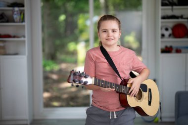 Çocuk evde akustik gitar çalıyor. Çocuk oturma odasında gitar çalışıyor. Genç gitarist içeride müzik öğreniyor. Müzik dersi sırasında gitar çalan bir çocuk. Çocuk odada gitar çalıyor.
