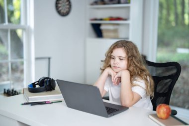 Çocuk evde bilgisayar ve kitaplarla ders çalışıyor. Çocuk, ev ödevi dersinde ödevini yapıyor. Evde öğrenim gören genç bir öğrenci. Çocuk okul masasında çalışmaya odaklanmış.