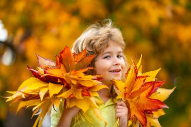 Sarı yaprağın yanındaki çocuk portresi. Sonbahar güz gününde sevimli çocuklar karşı karşıya gelir. Hayalperest çocukla sonbahar yeşilliği. Çocuklar için yapraklar