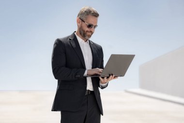 İş adamı dışarıda dizüstü bilgisayar kullanıyor. Dizüstü bilgisayar kullanan 40 'lı yaşlarda biri. Dizüstü bilgisayarı olan kendine güvenen bir iş adamı. İnternette iş. İş adamı laptoptaki verileri kontrol ediyor. Takım elbiseli iş adamı internette çalışıyor.